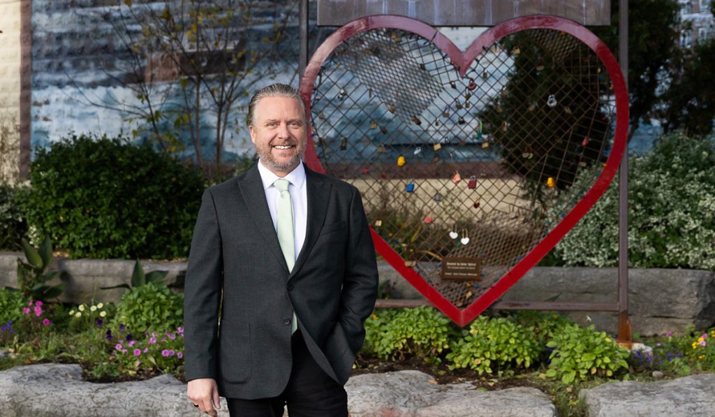 Jason Brass standing in front of the Love Acton Heart Art Sculpture and Mural in Acton, Ontario